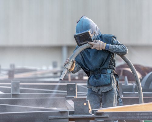 Sand blasting process, Industial worker using sand blasting process preparation cleaning surface on steel before painting in factory workshop.